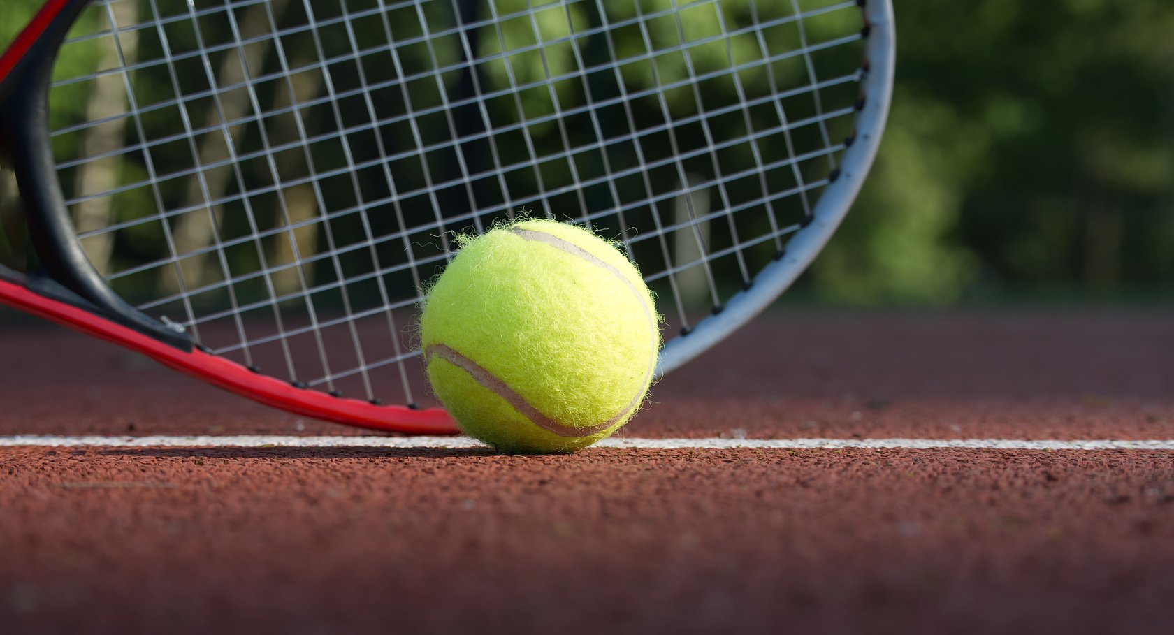 Tennis racquet and yellow tennis ball on outdoor court